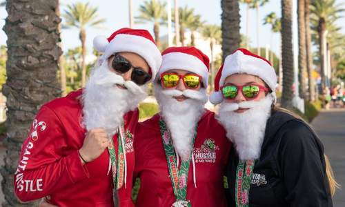 Three people dressed as Santa with sunglasses smiling at that camera during Santa Hustle on Galveston