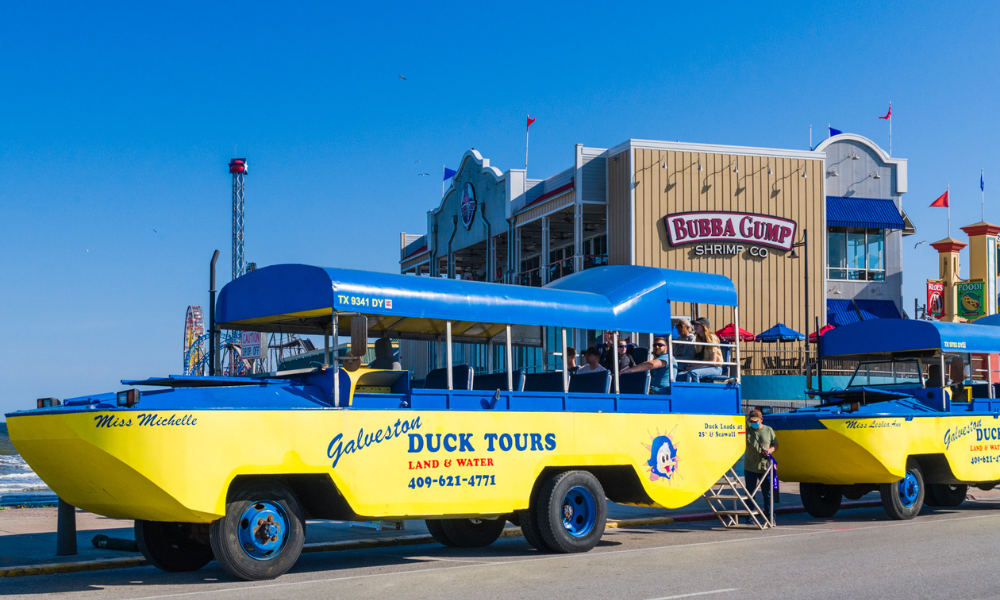 Two Galveston Duck Tour yellow and blue boats, parked in front of the Galveston Historic Pleasure Pier.